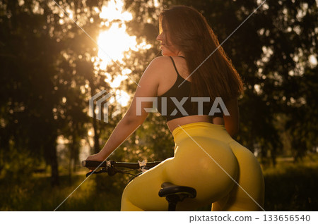 A Caucasian woman in yellow leggings and a crop top rides a bicycle in tights in the park. A Caucasian woman in yellow leggings and a crop top rides a bicycle in tights in the park. 133656540