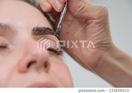 Caucasian woman getting eyebrow tinting procedure. Caucasian woman getting eyebrow tinting procedure. 133656553