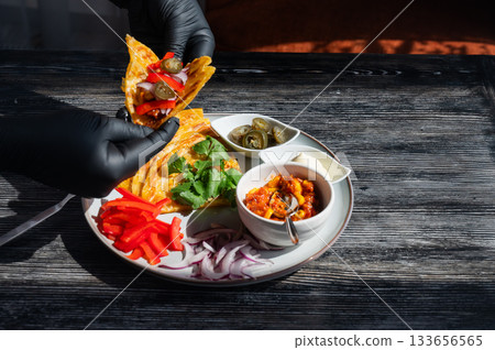 A chef wearing black gloves prepares fajitas.  133656565
