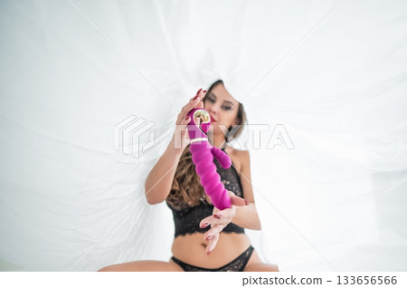 A woman in lingerie sits under a sheet and holds a vibrator.  133656566