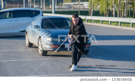 Caucasian man pulling a car with a rope. Caucasian man pulling a car with a rope. 133656608
