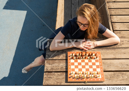 Caucasian woman playing chess outdoors. Caucasian woman playing chess outdoors. 133656620