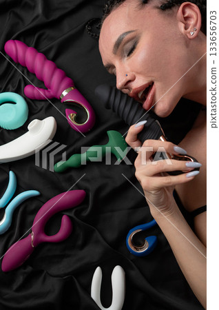 Portrait of Caucasian woman lying on bed among sex toys. Portrait of Caucasian woman lying on bed among sex toys. 133656703