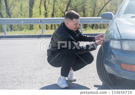 Caucasian man examines defects on his car body. Caucasian man examines defects on his car body. 133656719
