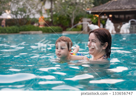 Caucasian woman holds son while swimming in pool on vacation. Caucasian woman holds son while swimming in pool on vacation. 133656747