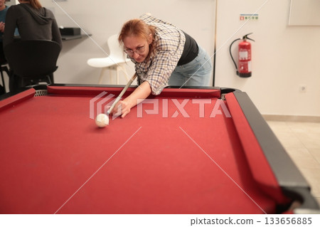 Woman playing pool aiming cue stick at white ball 133656885