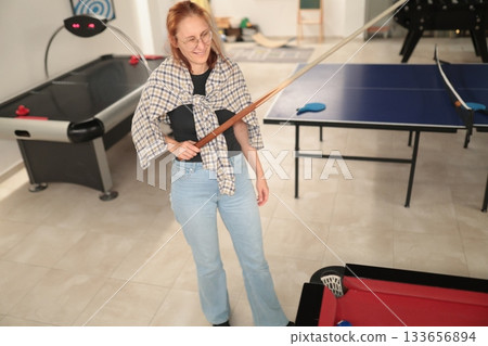 Woman holding pool cue ready to play billiards game 133656894