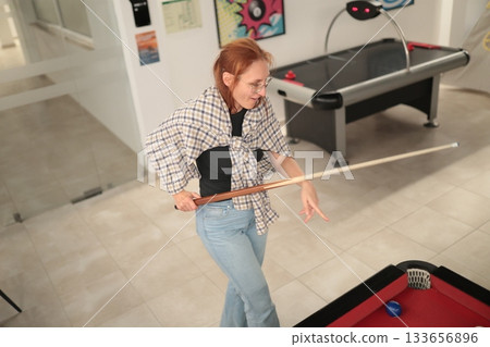 Woman playing billiards in game room concentrating on shot Woman playing billiards in game room concentrating on shot 133656896