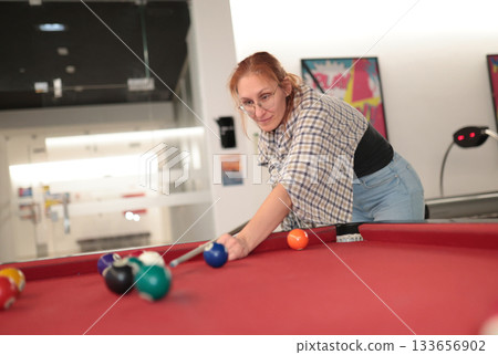 Woman playing pool aiming cue stick on red table 133656902