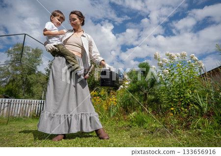 Caucasian woman and her son watering flowers in the garden.  133656916