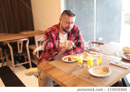 Man enjoying hotel breakfast eating a full meal Man enjoying hotel breakfast eating a full meal 133656960