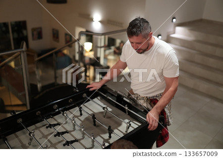 Adult man playing foosball game indoors Adult man playing foosball game indoors 133657009