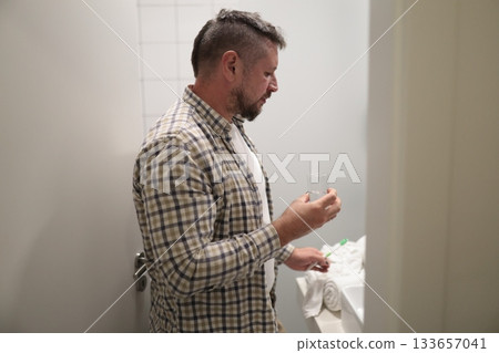 Man holding glass of water preparing to brush teeth Man holding glass of water preparing to brush teeth 133657041
