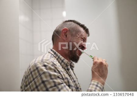 Man squinting eyes brushing teeth during morning routine 133657048