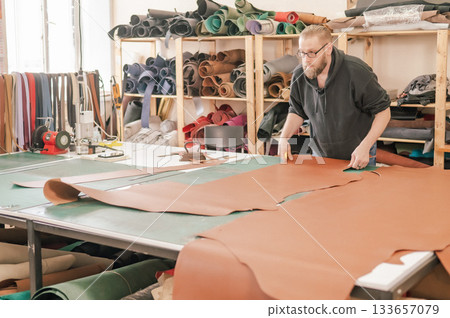 Caucasian bearded man working as a tanner in a workshop.  133657079