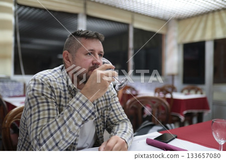Man drinking refreshment in restaurant bar setting Man drinking refreshment in restaurant bar setting 133657080