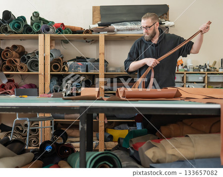 Caucasian bearded man working as a tanner in a workshop. Caucasian bearded man working as a tanner in a workshop. 133657082