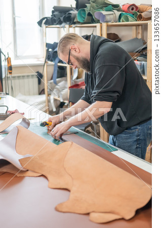 Caucasian bearded man working as a tanner in a workshop. Caucasian bearded man working as a tanner in a workshop. 133657086