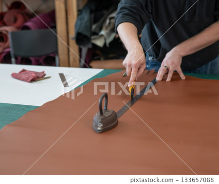Leatherworker measuring and cutting leather in workshop.  133657088