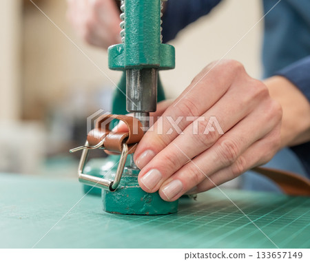A woman attaches accessories to a leather belt. Leatherworker's workshop.  133657149