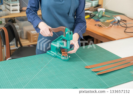 A woman attaches accessories to a leather belt. Leatherworker's workshop.  133657152