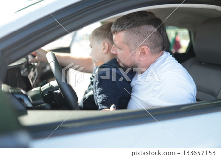 Father teaching son driving car on sunny day 133657153