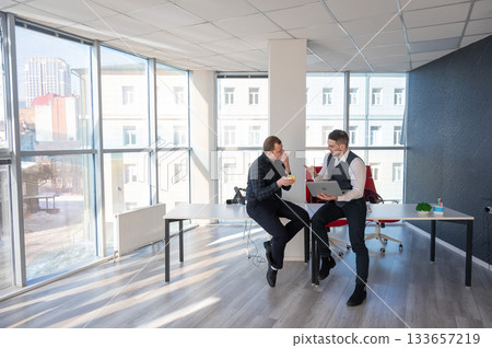Two Caucasian men discussing work in an office. Businessman with a hearing aid.  133657219