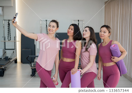 Two Caucasian and two Asian women take a selfie after a Pilates workout. Two Caucasian and two Asian women take a selfie after a Pilates workout. 133657344