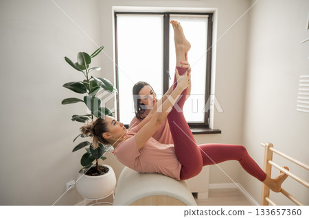 A trainer adjusts woman on a Ladder Barrel. Personal training.  133657360