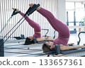 Two young asian women doing pilates exercises on a reformer.  133657361