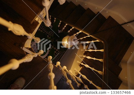 A wooden spiral staircase with white railings and pendant lights in the center creates a cozy interior. A wooden spiral staircase with white railings and pendant lights in the center creates a cozy interior. 133657466