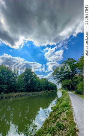 Dramatic sky above meandering canal with contrasting light and darkness 133657643