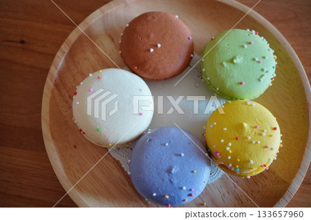 A bird's-eye view of five colorful macarons arranged on a wooden plate. A sweet image that stands out with its pastel colors and cute decorations. A bird's-eye view of five colorful macarons arranged on a wooden plate. A sweet image that stands out with its pastel colors and cute decorations. 133657960
