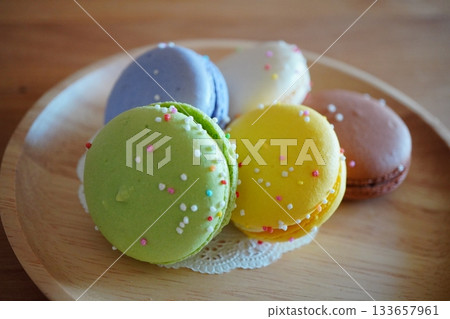 The green and yellow macarons stand out in the center of this composition. The soft light and the warmth of the wooden plate accentuate the sweets' charm. The green and yellow macarons stand out in the center of this composition. The soft light and the warmth of the wooden plate accentuate the sweets' charm. 133657961