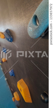 An indoor climbing wall with colorful holds set at children's height is located in an indoor playground with a soft, safe surface. Concept: children's activities, rock climbing, playground safety. 133657972