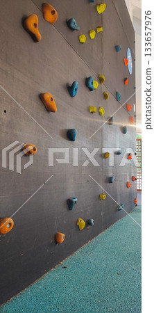 An indoor climbing wall with colorful holds set at children's height is located in an indoor playground with a soft, safe surface. Concept: children's activities, rock climbing, playground safety. 133657976