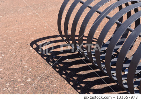A bicycle rack casts a shadow on the ground on a sunny day. Concept: abstraction, geometry, cycling elements, sustainable consumption, carbon footprint. 133657978