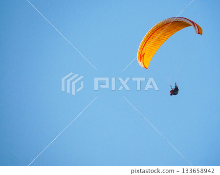 Paraglider flying in blue sky. 133658942