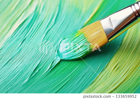 Paintbrush applying vibrant green paint onto canvas, showcasing texture and technique in a creative workspace with various shades 133659952