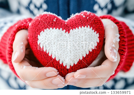 Holding a knitted heart in hands during a snowy winter day near a cozy fireplace 133659971