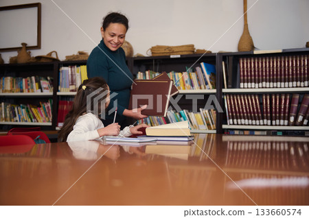 Friendly Teacher Helps Student With Books in Busy Library During Study Time Friendly Teacher Helps Student With Books in Busy Library During Study Time 133660574