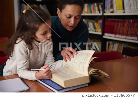 Tutor Helps Child Read In Library During Study Session 133660577