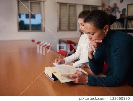 Focused Reading Session With Woman Reading a Book At Library Table During Study 133660580