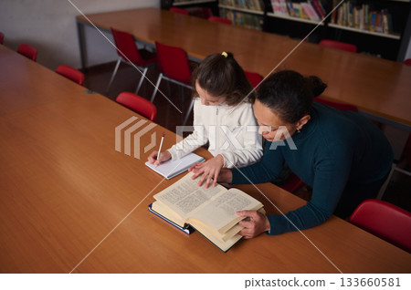 Teacher Helps Student Read in Library During Study Session, Fostering Learning and Focus 133660581