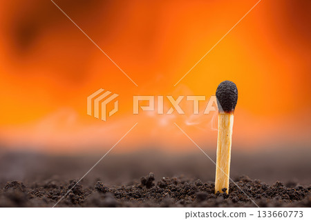Single burnt matchstick stands upright in dark soil, with smoke rising gently against vibrant orange background, symbolizing resilience and aftermath in dramatic scene Single burnt matchstick stands upright in dark soil, with smoke rising gently against vibrant orange background, symbolizing resilience and aftermath in dramatic scene 133660773