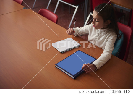 Young Girl Studying At A Table With Notebook And Blue Book In Classroom Setting 133661310