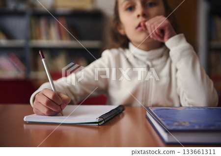 Child Writing in Library During Quiet Study Hour With Books Nearby 133661311
