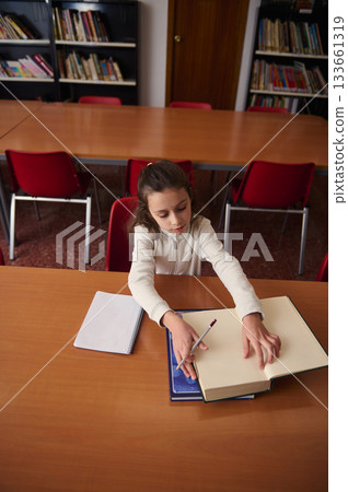 Young Girl Studying At Library Table With Open Books And Notebook 133661319