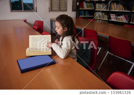 Young Girl Reading A Book At Library Table In School Library During Quiet Study Time 133661326