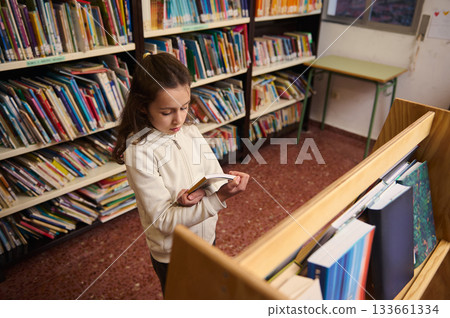 Little Girl Reading a Book in a Public School Library for Book Day Celebration 133661334